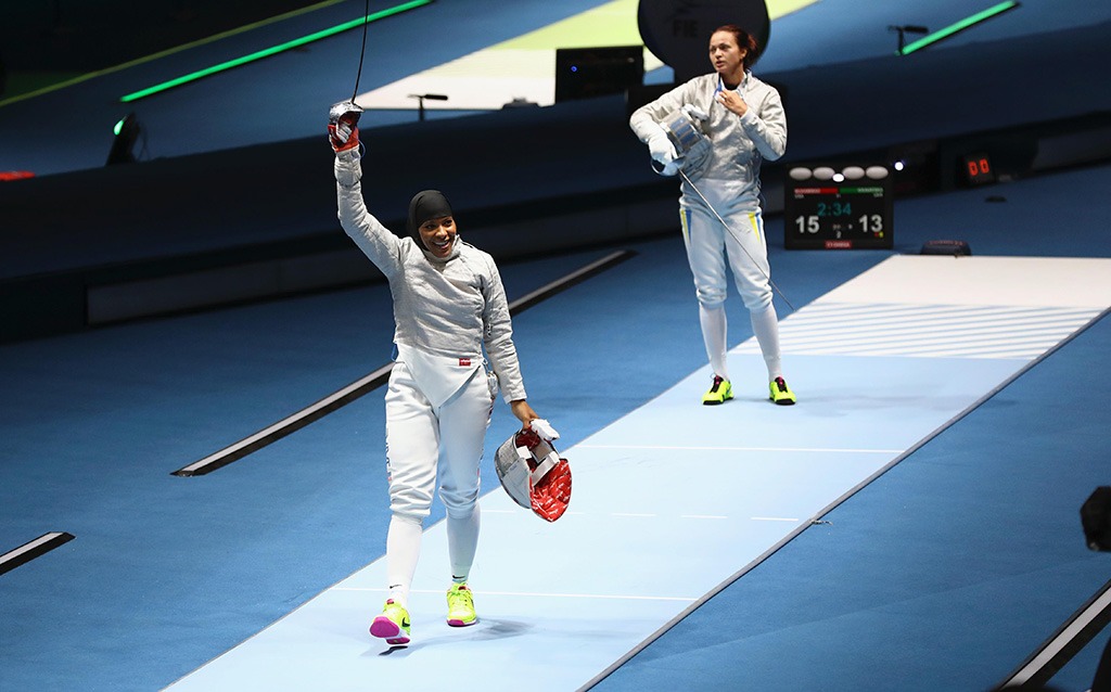 Ibtihaj Muhammad smiles as she takes off her mask and raises her sabre in victory