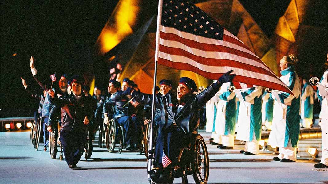 In her wheelchair, Candace Cable carries the U.S. flag into the stadium, with her left arm raised