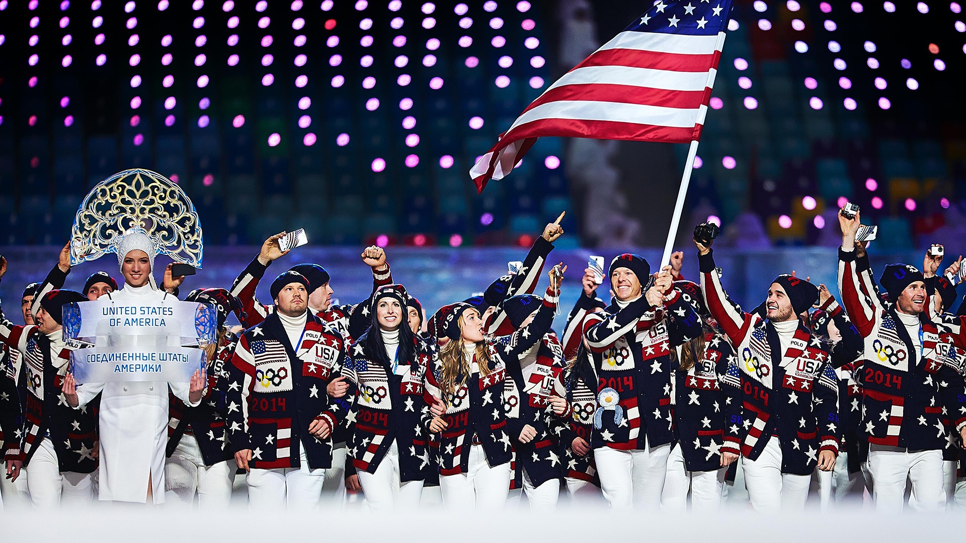 Todd Lockwick smiles and holds high the U.S. flag as Team USA athletes wave