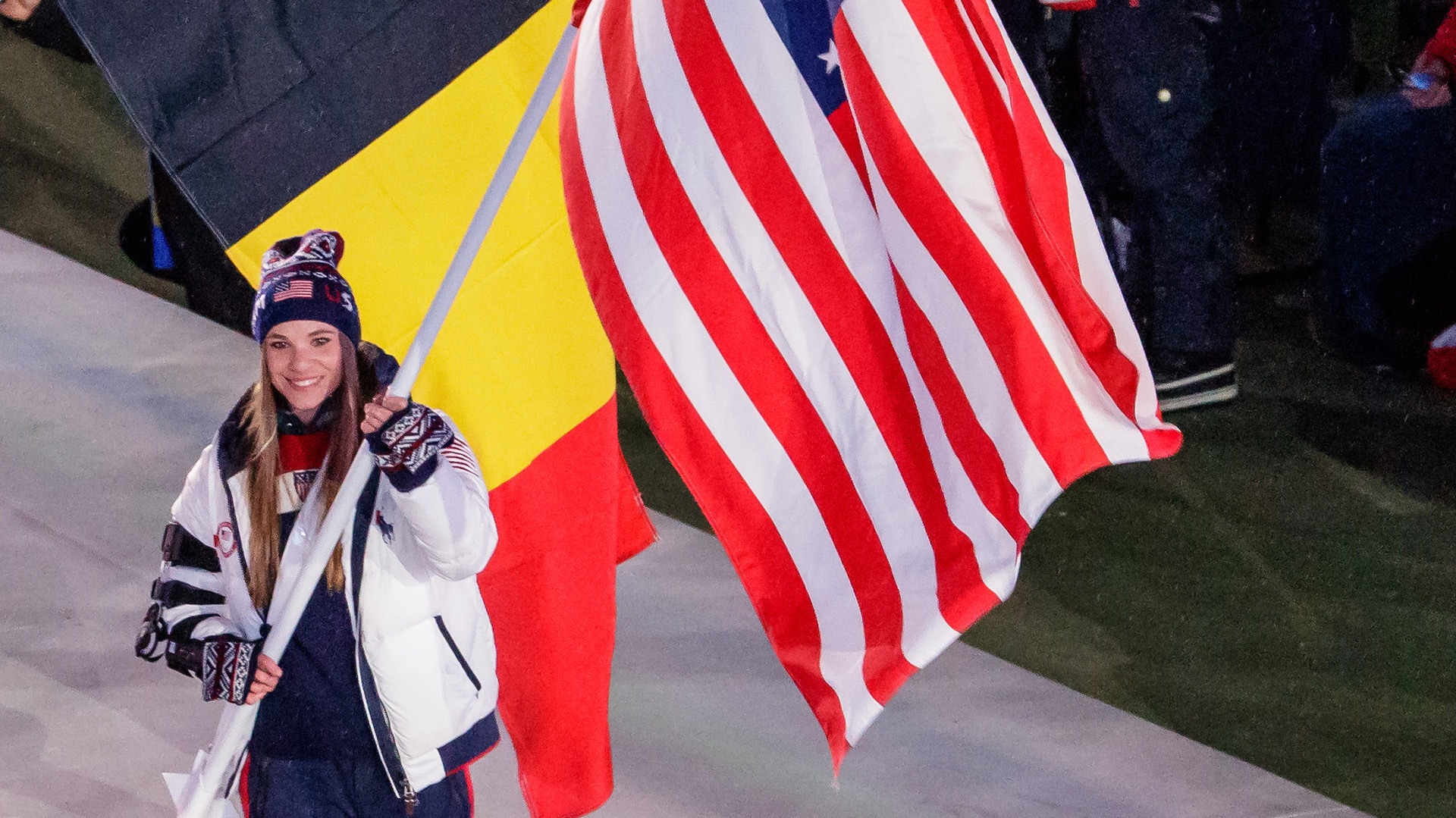 Oksana Masters smiles and holds the U.S. flag as she walks into the stadium