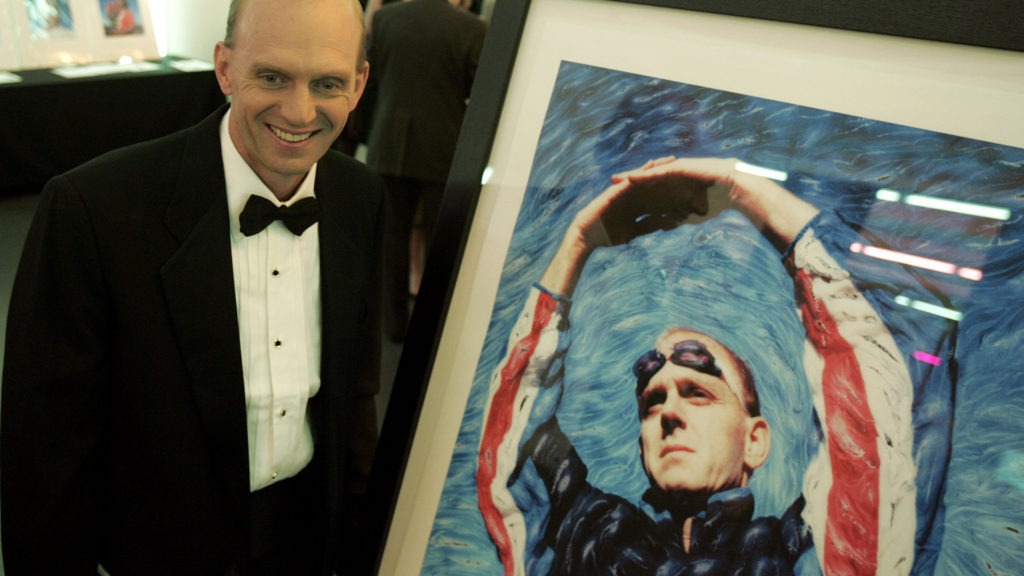 Rowdy Gaines in a tuxedo standing next to a portrait from his swimming career