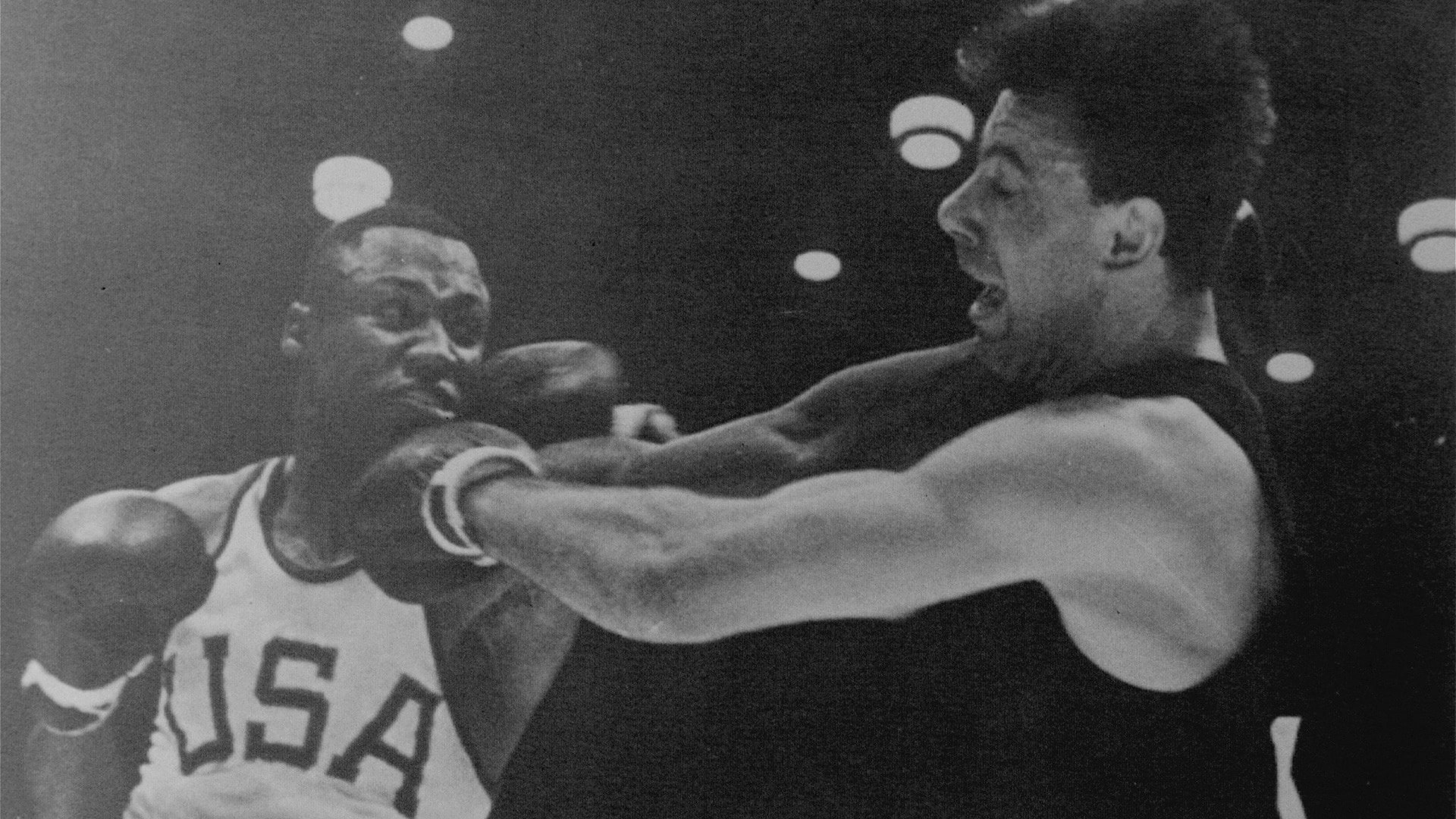 Joe Frazier is punching with his left fish and has his right arm cocked and ready to punch German Hans Huber in the gold-medal bout.
