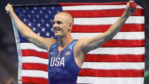 Sam Kendricks beams while holding an American flag behind his shoulders