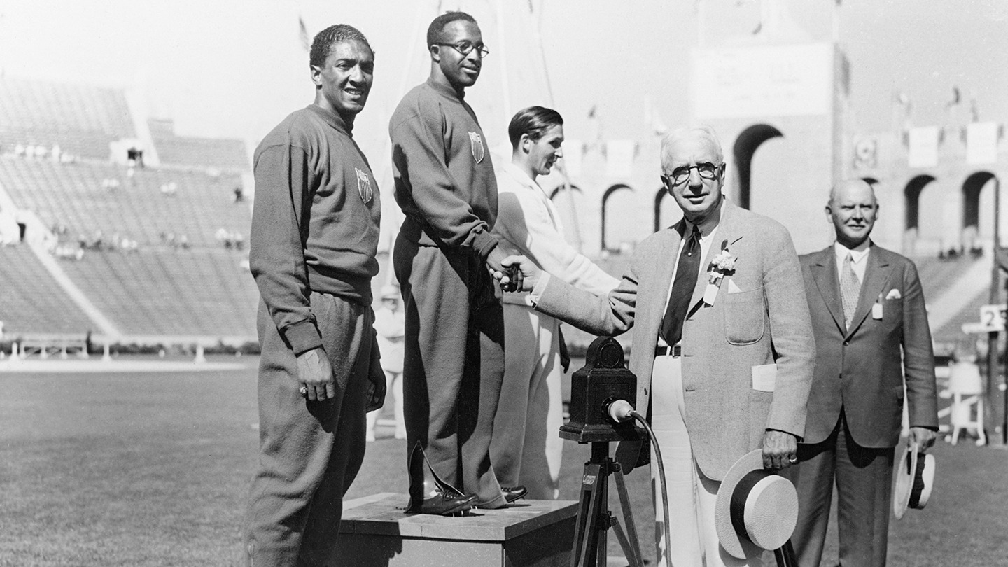 Eddie Tolan proudly stands atop the podium for the medal presentation for the 100 meter race at Los Angeles 1932