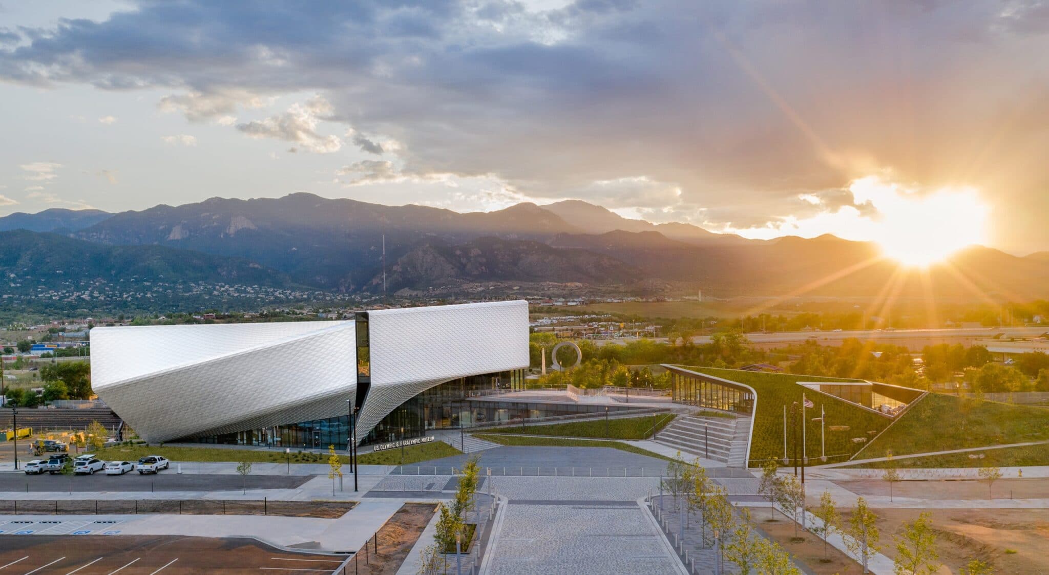 The sun sets over the mountains behind the exterior of the United States Olympic and Paralympic Museum.