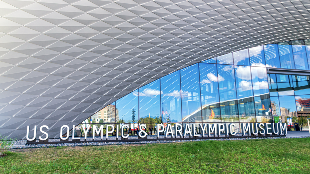 External shot of United States Olympic and Paralympic Museum with clouds and sky reflected in exterior.