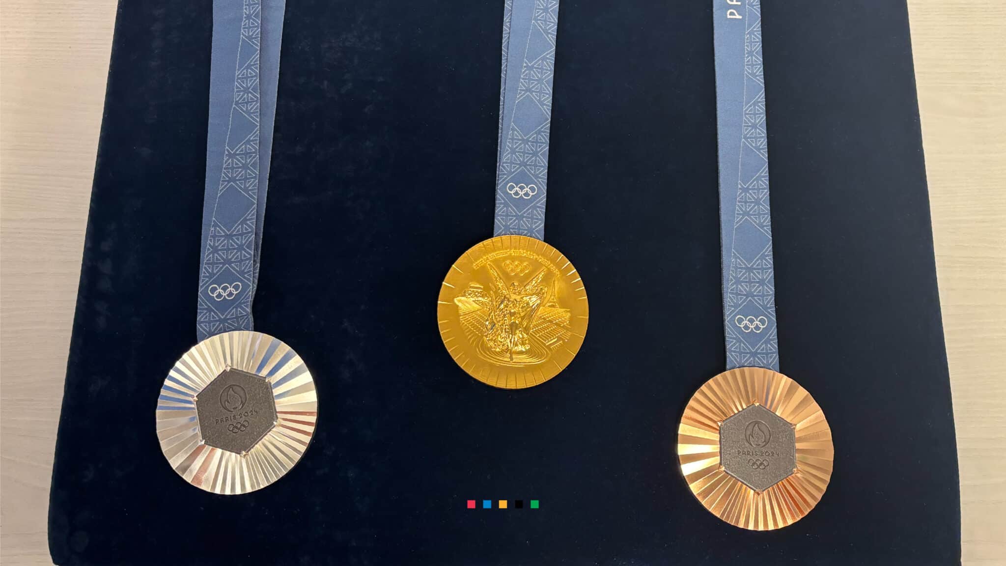 The 2024 Paris Olympic medals displayed on a felt blue background. Gold medal in the center with bronze and silver medal on the side with their iron piece side showing